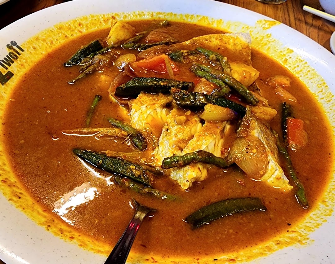 A vibrant close-up of a large plate of fish curry with vegetables in a rich, spicy sauce.