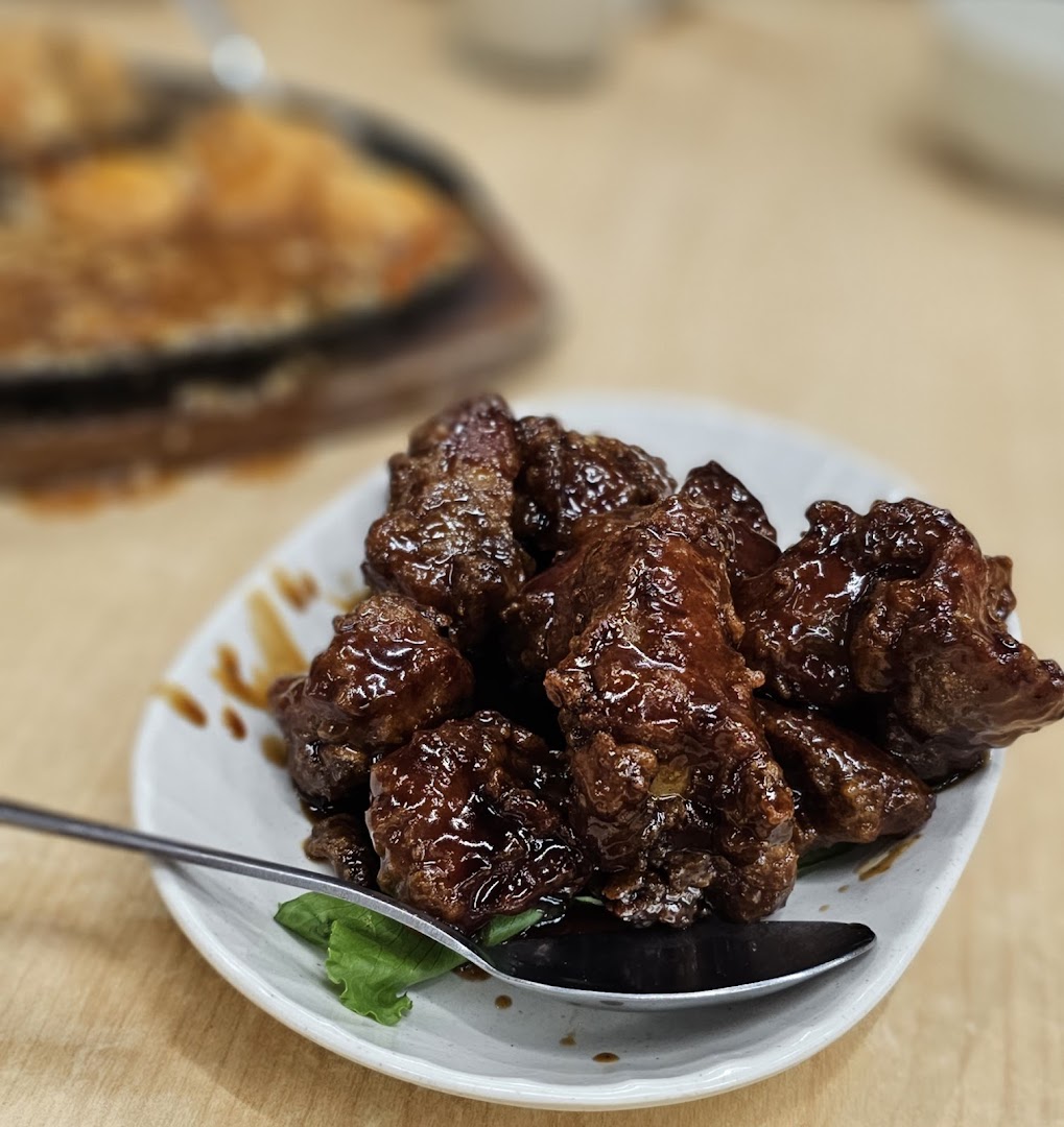 A close-up of a plate of glistening, dark glazed meat pieces with a serving spoon.