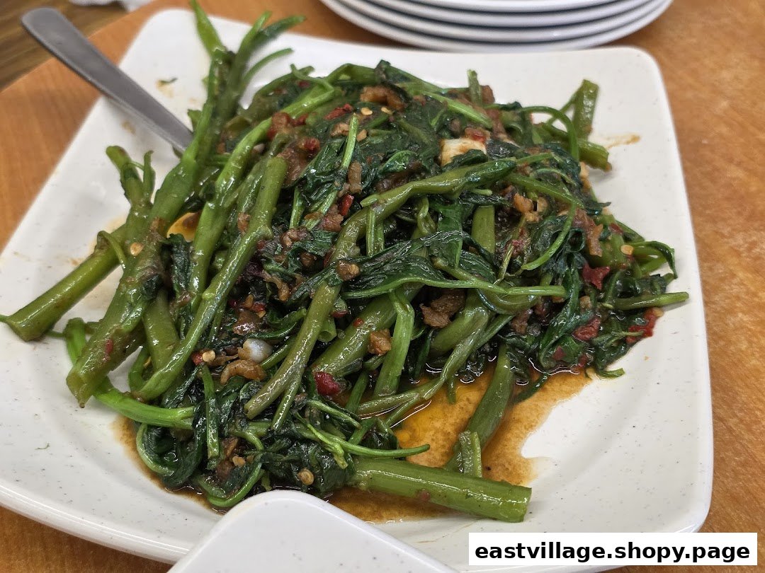 A close-up of a plate of stir-fried kangkong with chili and garlic, served on a white rectangular dish.