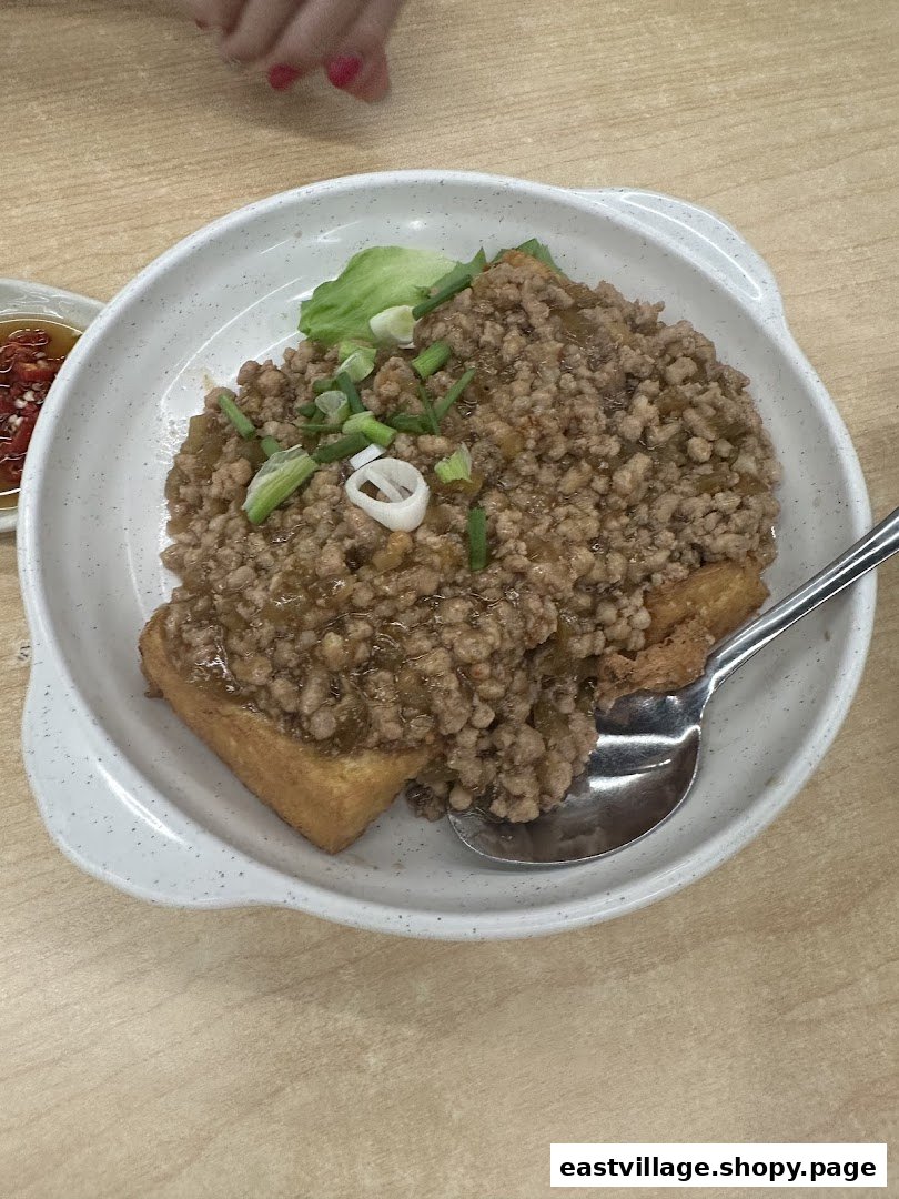 A close-up of a dish featuring fried tofu topped with minced meat and spring onions.