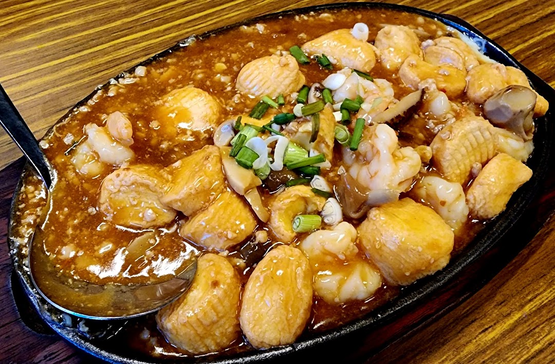 A sizzling hotplate dish featuring golden tofu, succulent prawns, squid, and mushrooms in a rich savory sauce.