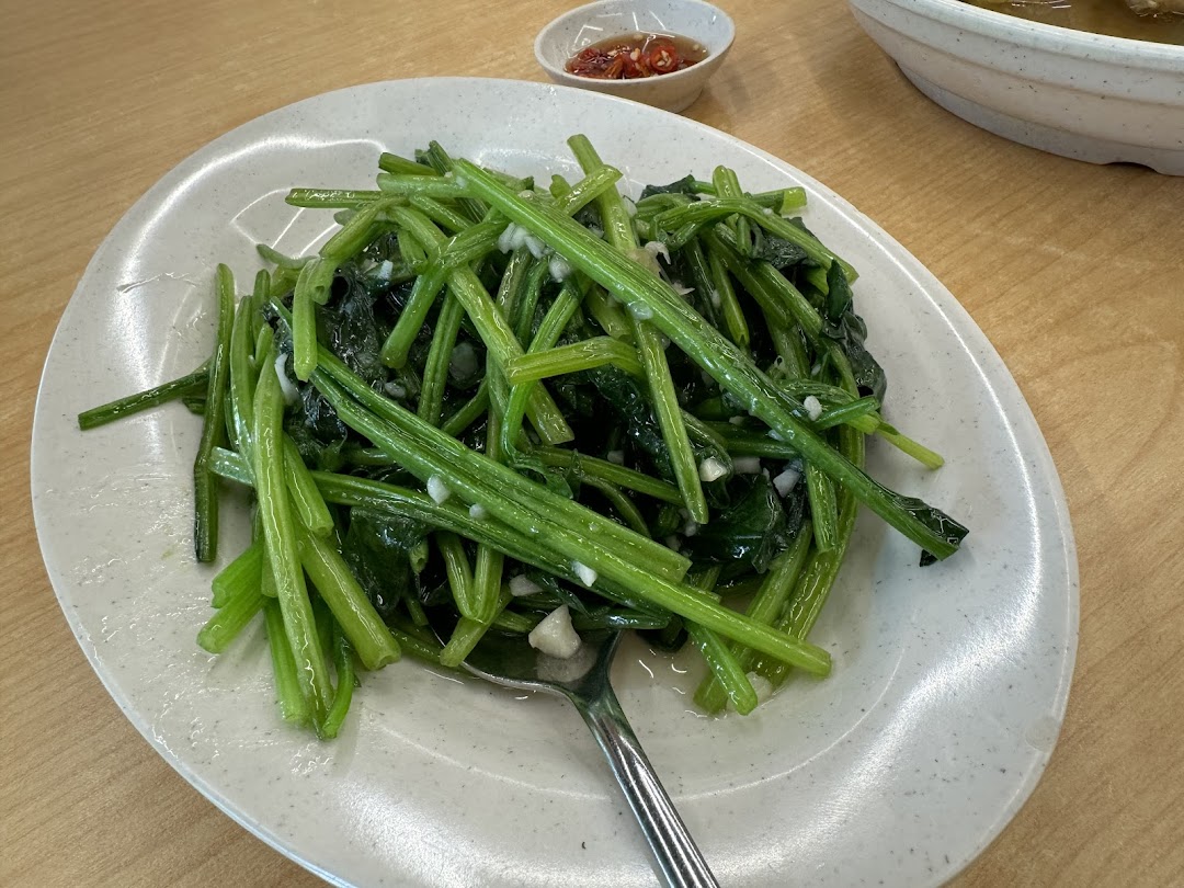 A plate of vibrant green stir-fried vegetables with garlic, accompanied by a chili dip.