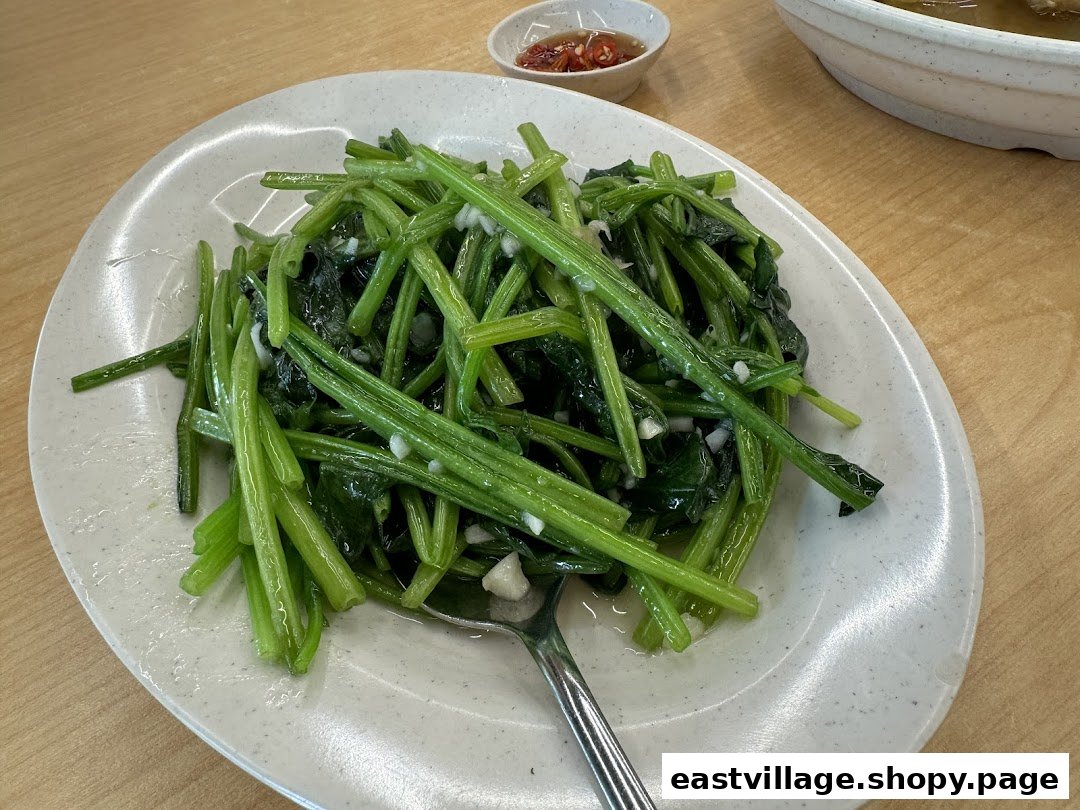 A plate of vibrant green stir-fried vegetables with garlic, accompanied by a chili dip.