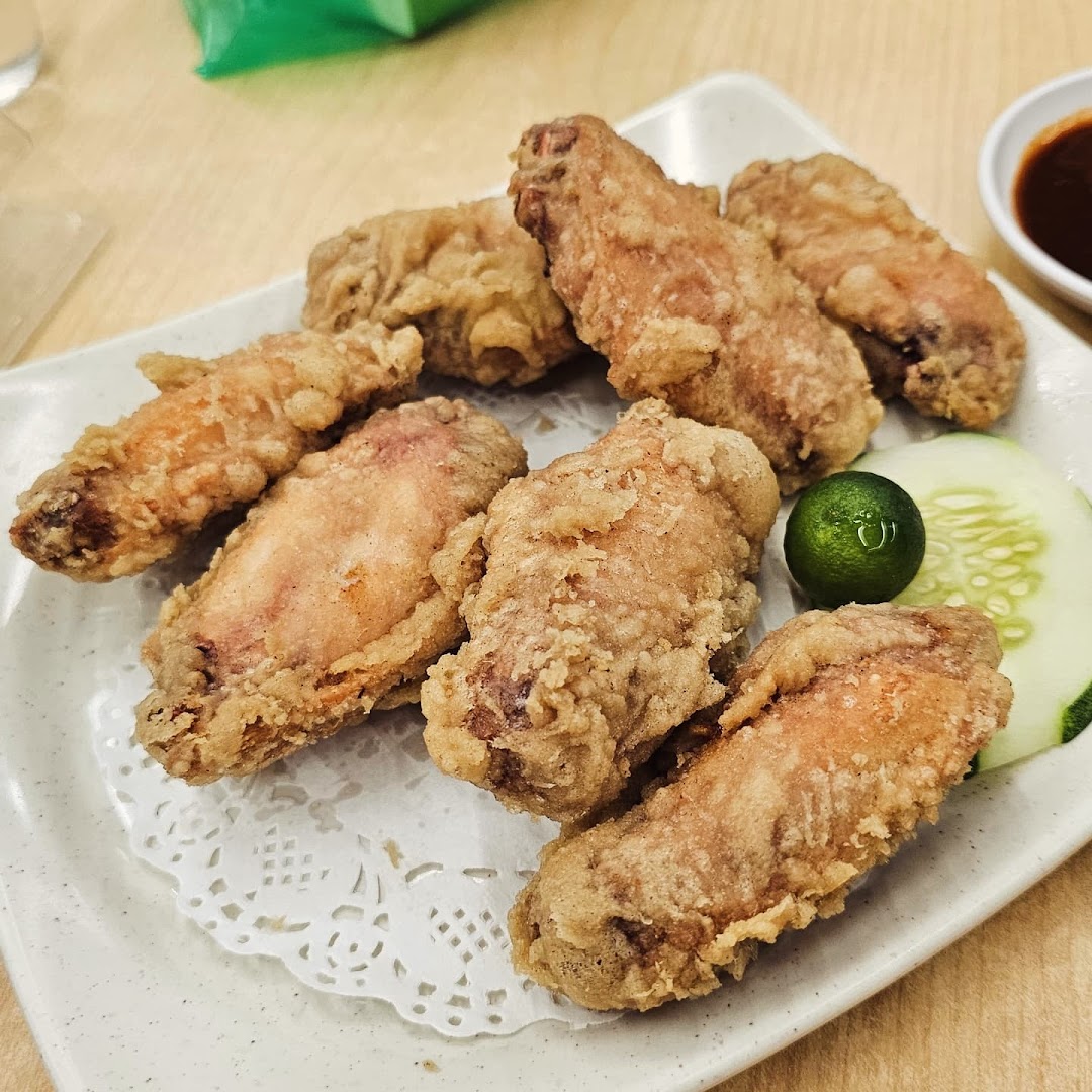 A plate of golden crispy fried chicken wings served with a lime and cucumber slice.