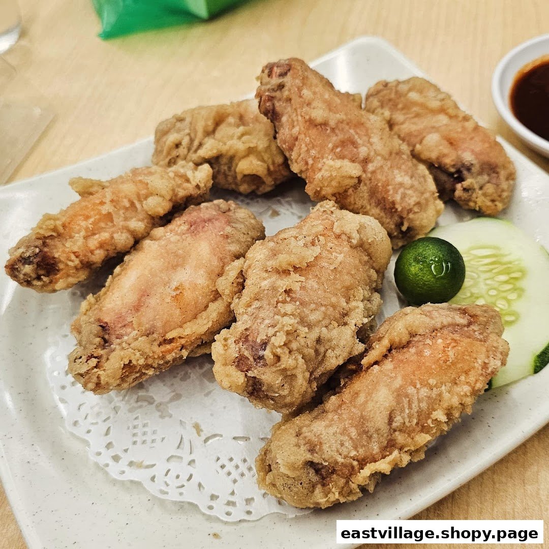 A plate of golden crispy fried chicken wings served with a lime and cucumber slice.