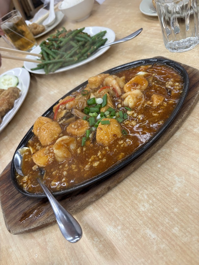 A sizzling hot plate of prawns and tofu in rich sauce, with side dishes on a wooden table.