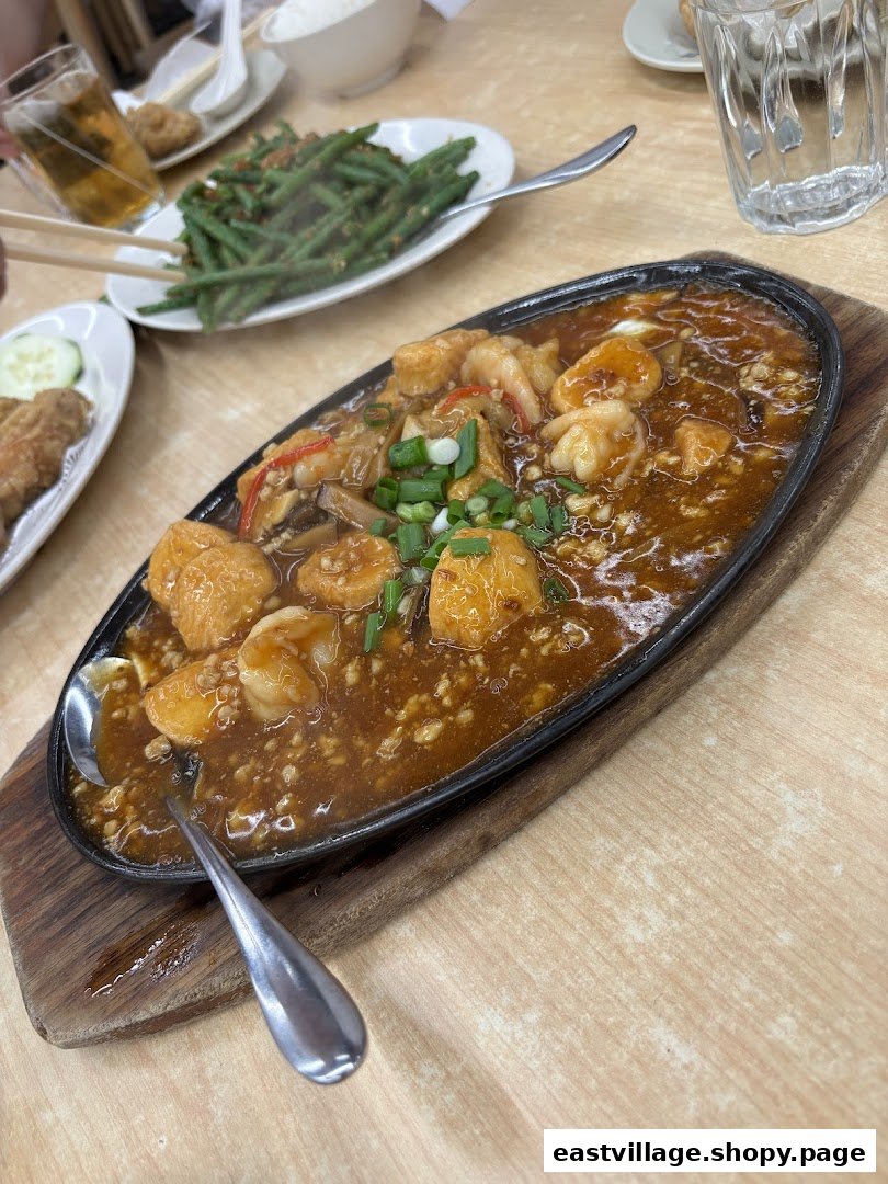 A sizzling hot plate of prawns and tofu in rich sauce, with side dishes on a wooden table.
