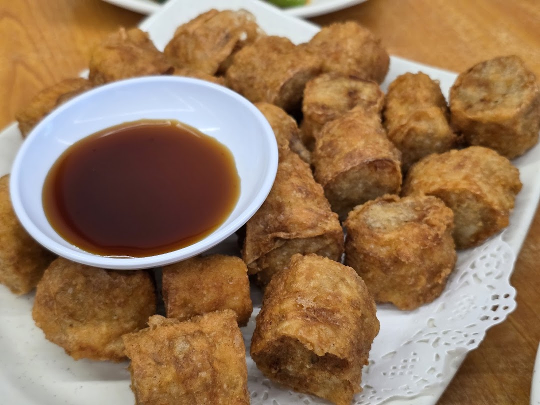 A close-up of crispy deep-fried Ngoh Hiang or similar Chinese rolls with a dipping sauce.
