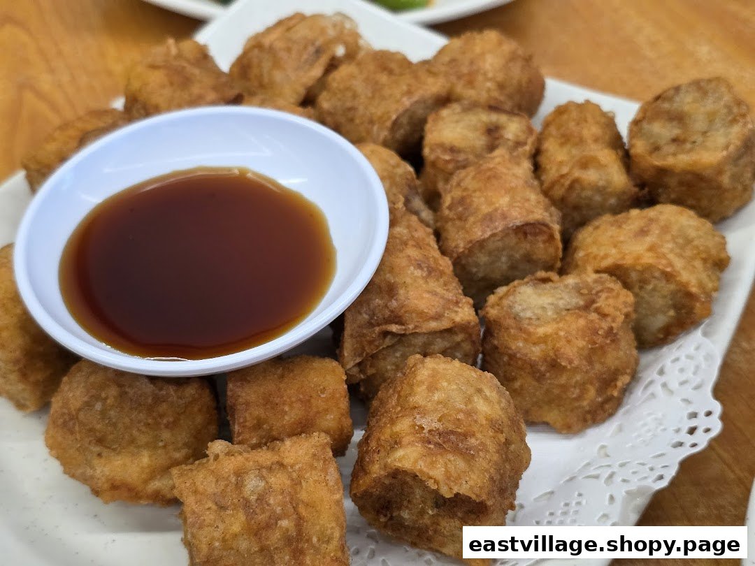 A close-up of crispy deep-fried Ngoh Hiang or similar Chinese rolls with a dipping sauce.