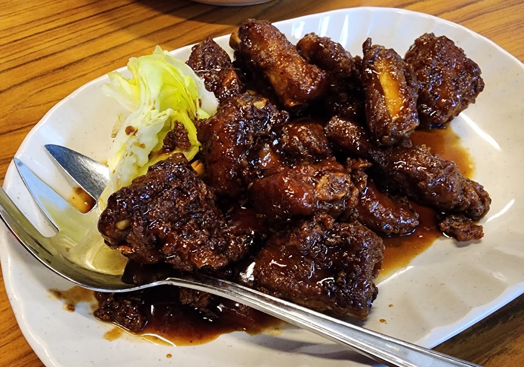 A plate of dark glazed ribs or chicken pieces with a side of fresh lettuce and a serving fork.