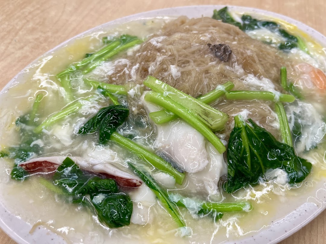 A close-up of a plate of seafood noodles with gravy, vegetables, and egg.
