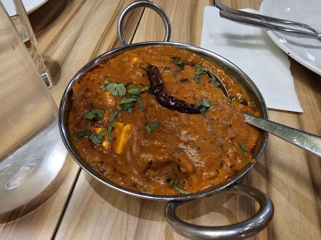 A vibrant Indian curry dish, possibly paneer, served in a traditional karahi on a wooden table.