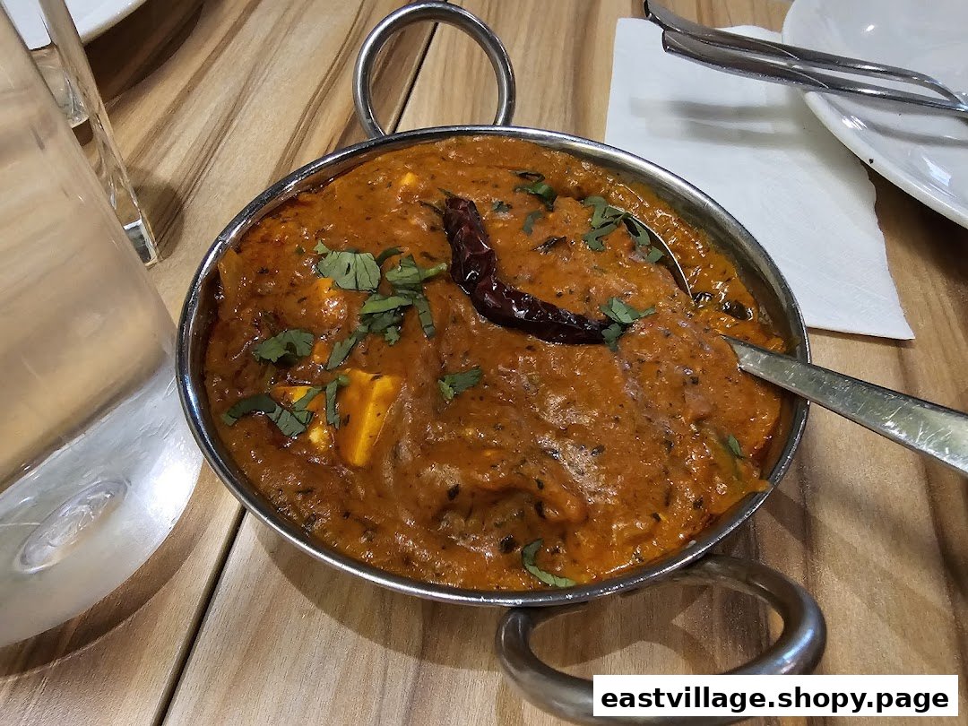 A vibrant Indian curry dish, possibly paneer, served in a traditional karahi on a wooden table.