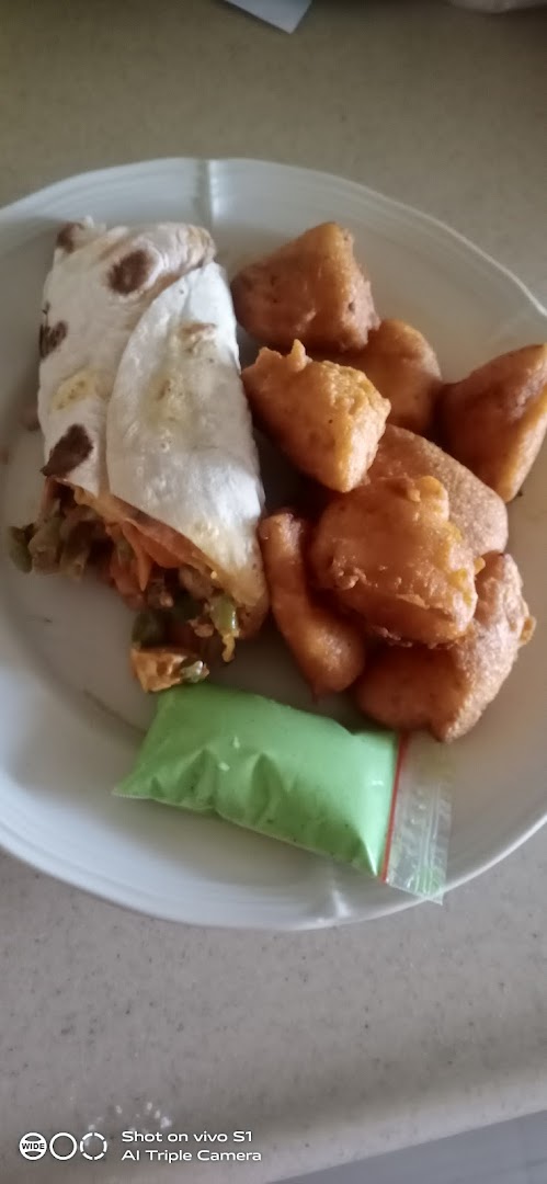 A plate featuring a savory wrap, golden fried snacks, and a vibrant green dipping sauce.