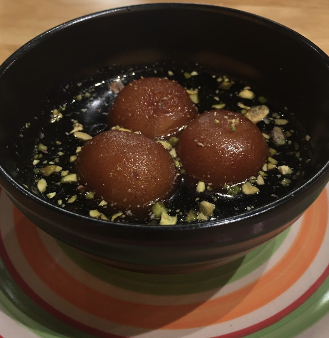 A bowl of traditional Indian gulab jamun dessert with pistachio garnish.