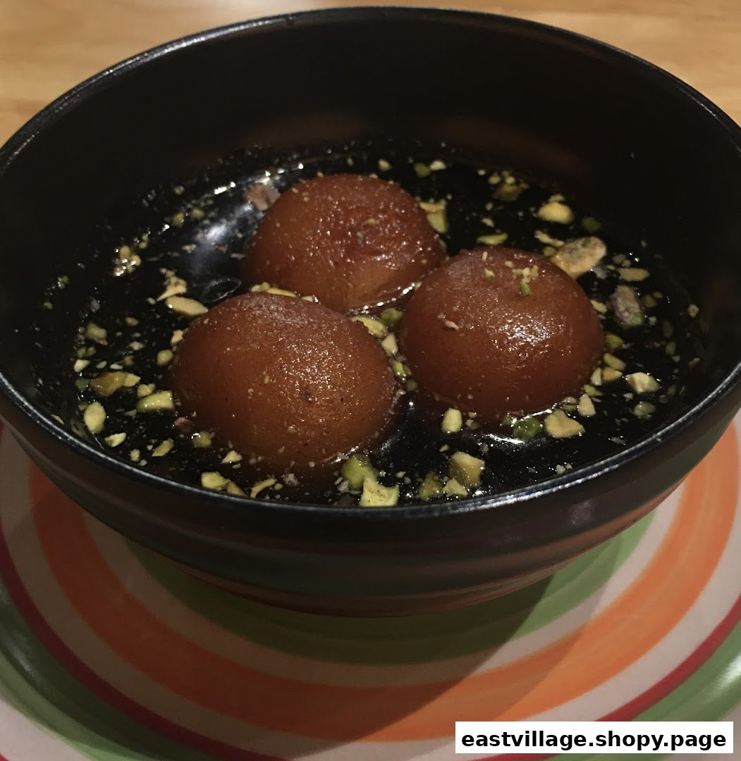A bowl of traditional Indian gulab jamun dessert with pistachio garnish.
