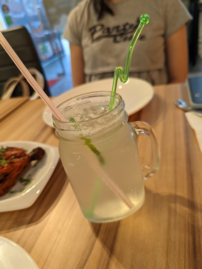 A refreshing drink in a mason jar with a colorful straw, alongside a plate of Indian food.