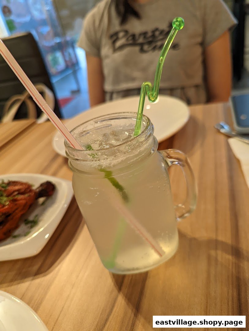 A refreshing drink in a mason jar with a colorful straw, alongside a plate of Indian food.