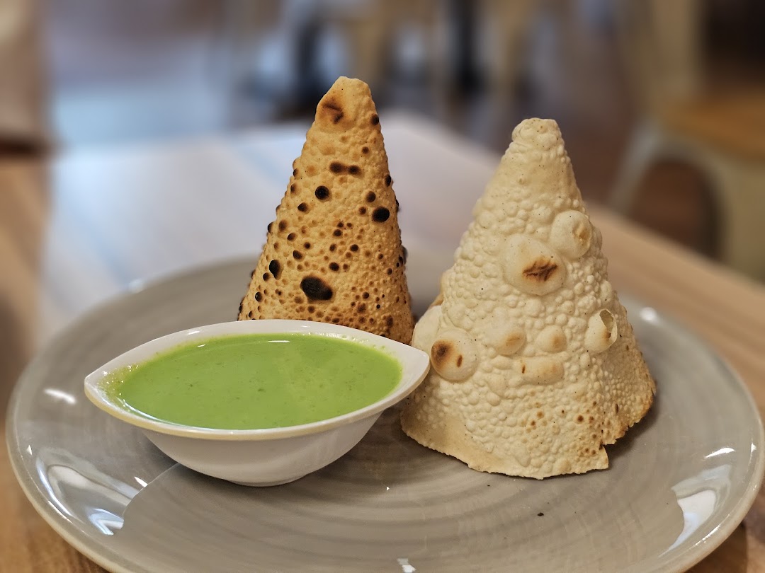 Two conical papadums, one plain and one roasted, served with a vibrant green chutney on a plate.