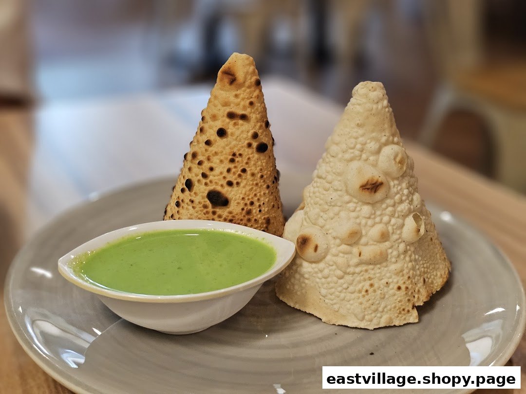 Two conical papadums, one plain and one roasted, served with a vibrant green chutney on a plate.