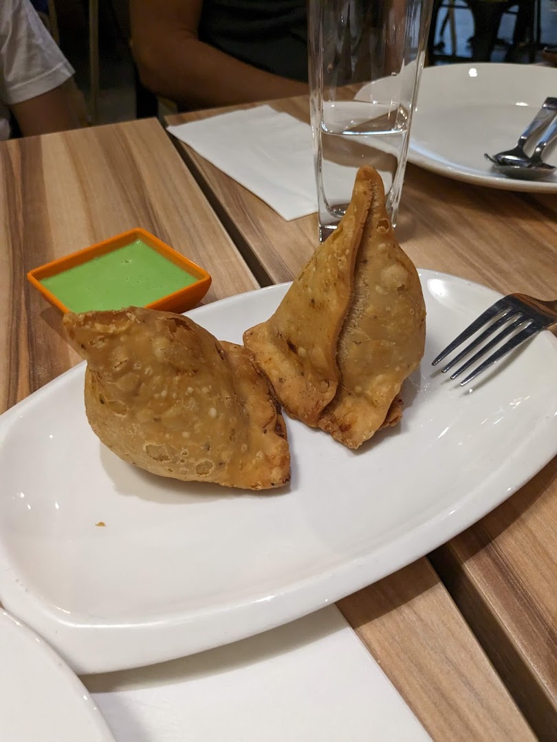 Two golden-brown samosas with green chutney on a white plate, ready to be enjoyed.