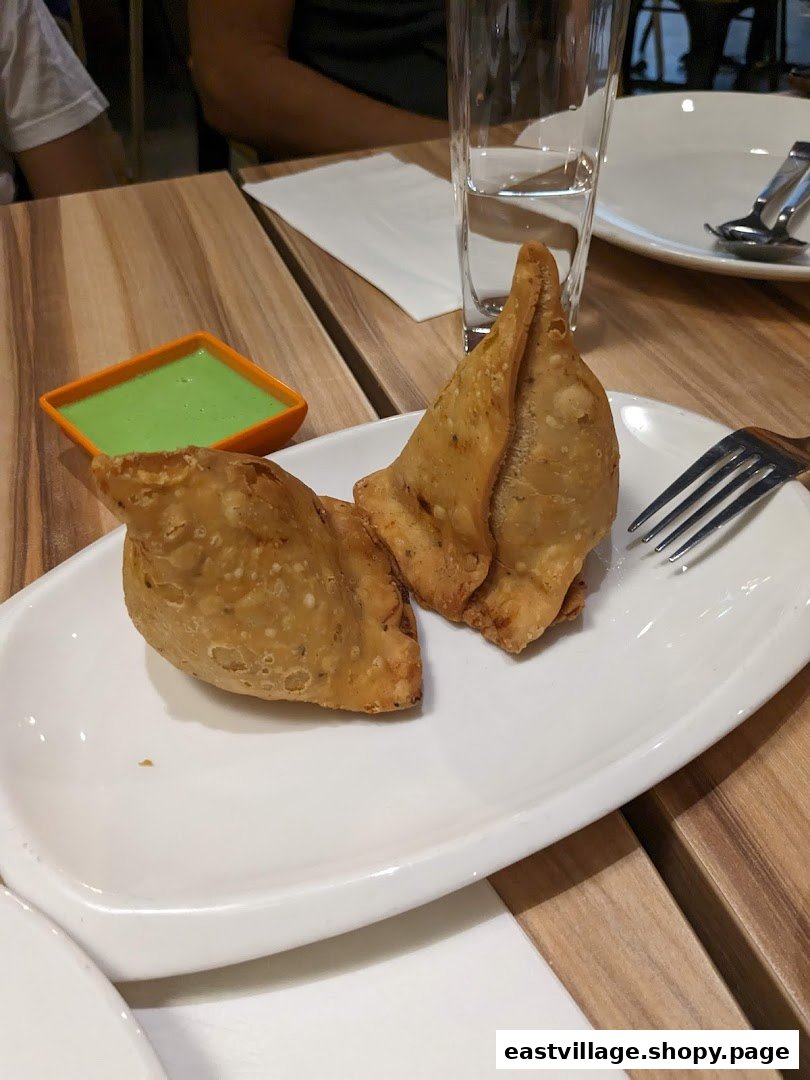Two golden-brown samosas with green chutney on a white plate, ready to be enjoyed.