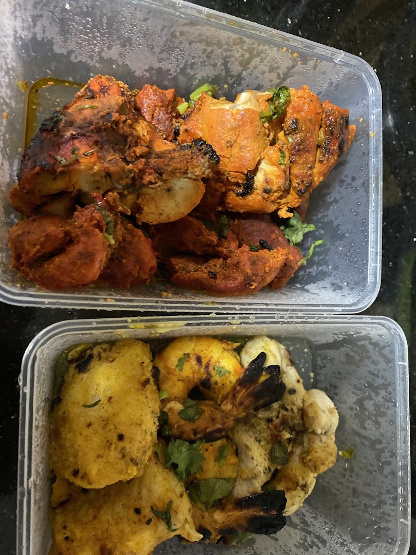 Two takeout containers filled with various tandoori-style meats and seafood, including chicken and prawns.