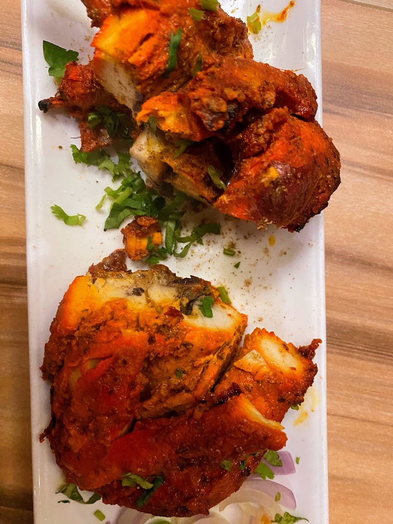 Close-up of vibrant red tandoori chicken pieces garnished with fresh cilantro on a white plate.