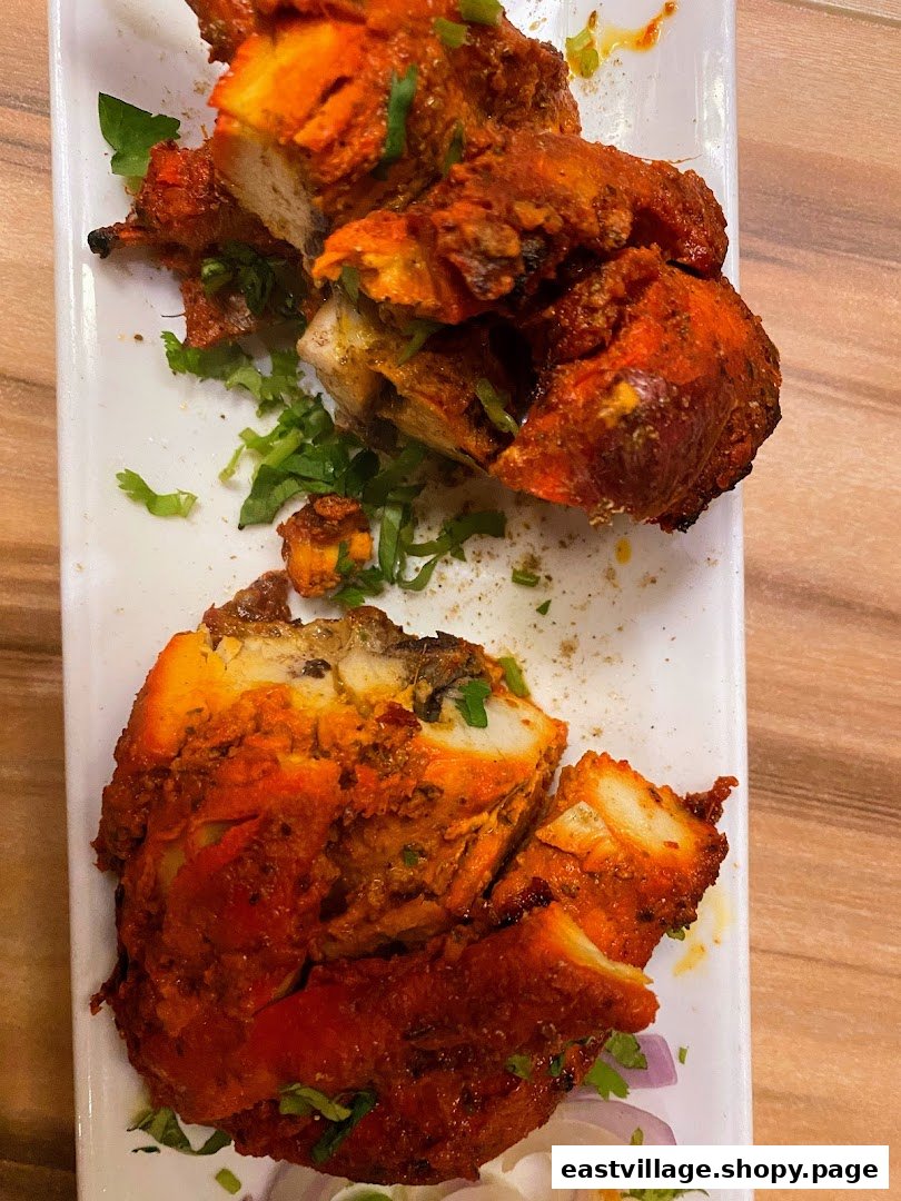 Close-up of vibrant red tandoori chicken pieces garnished with fresh cilantro on a white plate.