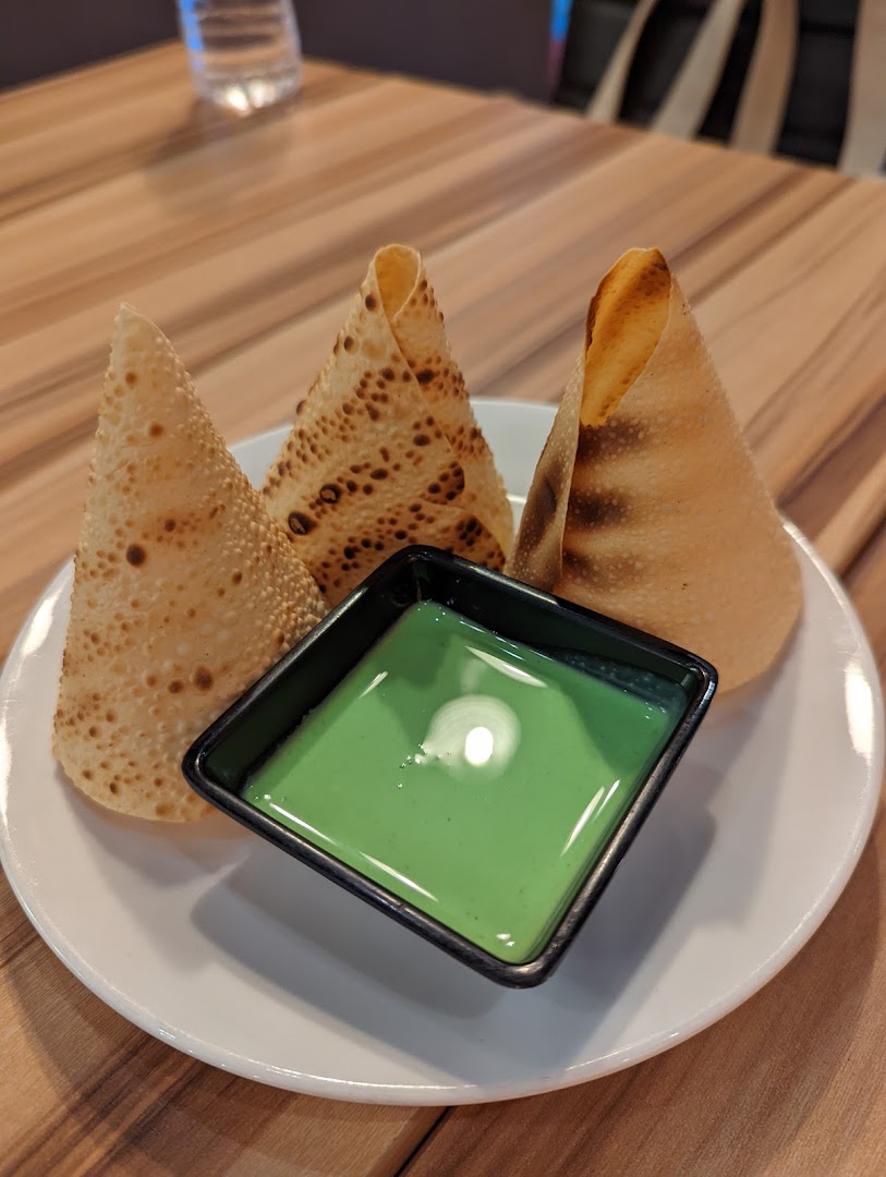 Three crispy papadums served with a vibrant green dipping sauce on a white plate.