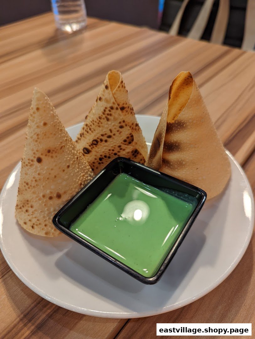 Three crispy papadums served with a vibrant green dipping sauce on a white plate.