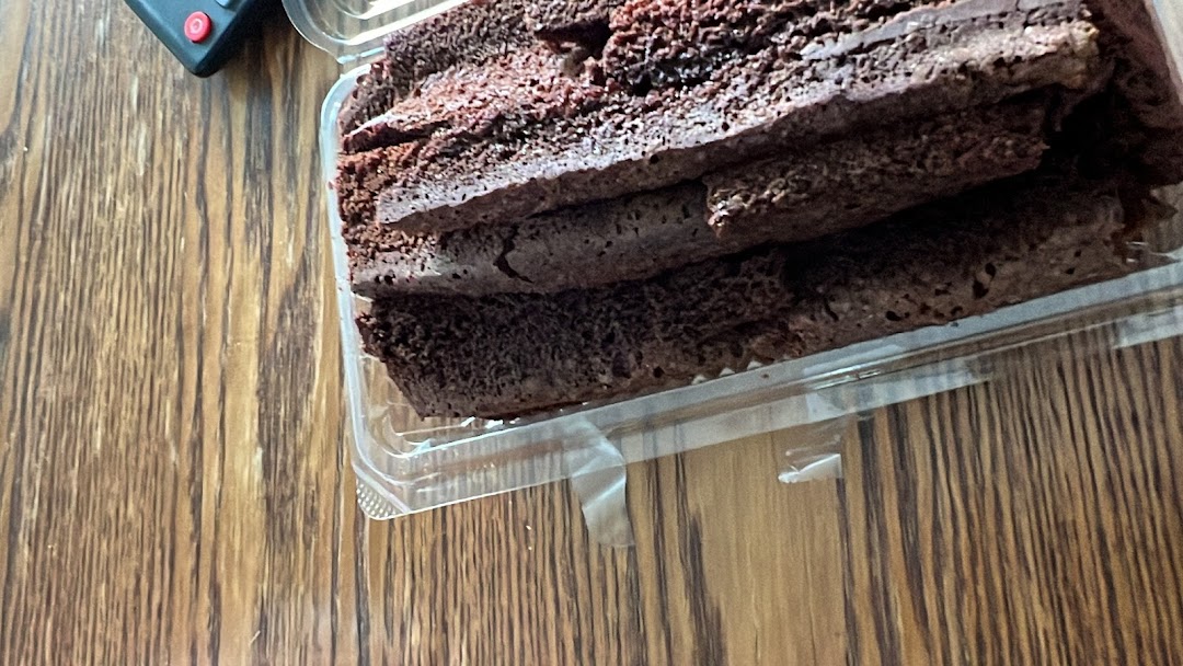 Slices of chocolate cake or brownie in a clear plastic container on a wooden surface.