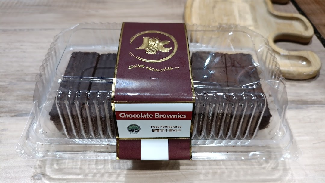 A clear plastic container of J C Bakery chocolate brownies on a wooden surface.