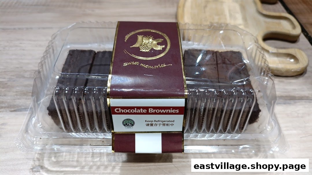 A clear plastic container of J C Bakery chocolate brownies on a wooden surface.