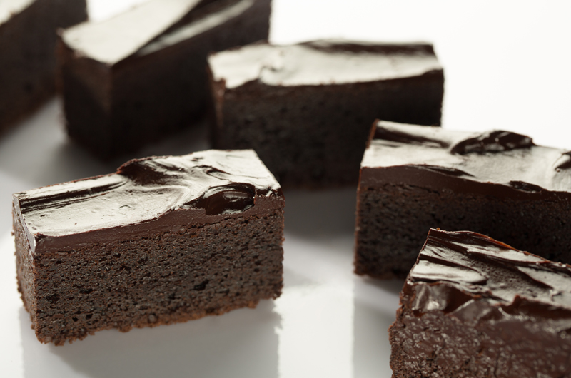 Several rich chocolate brownies with glossy frosting are arranged on a white surface.