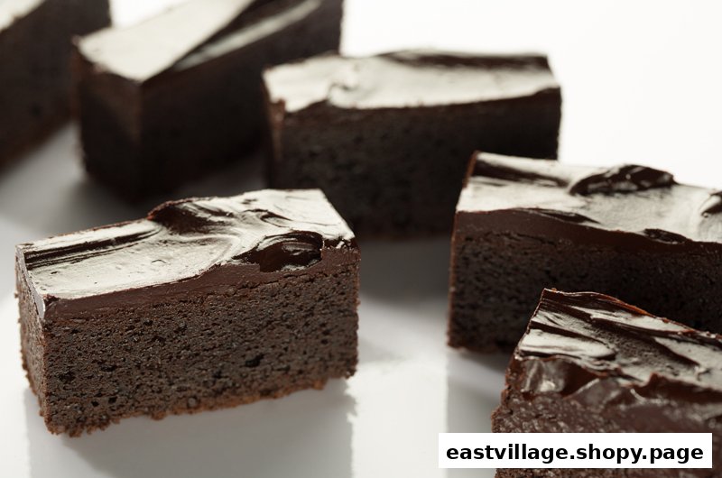 Several rich chocolate brownies with glossy frosting are arranged on a white surface.