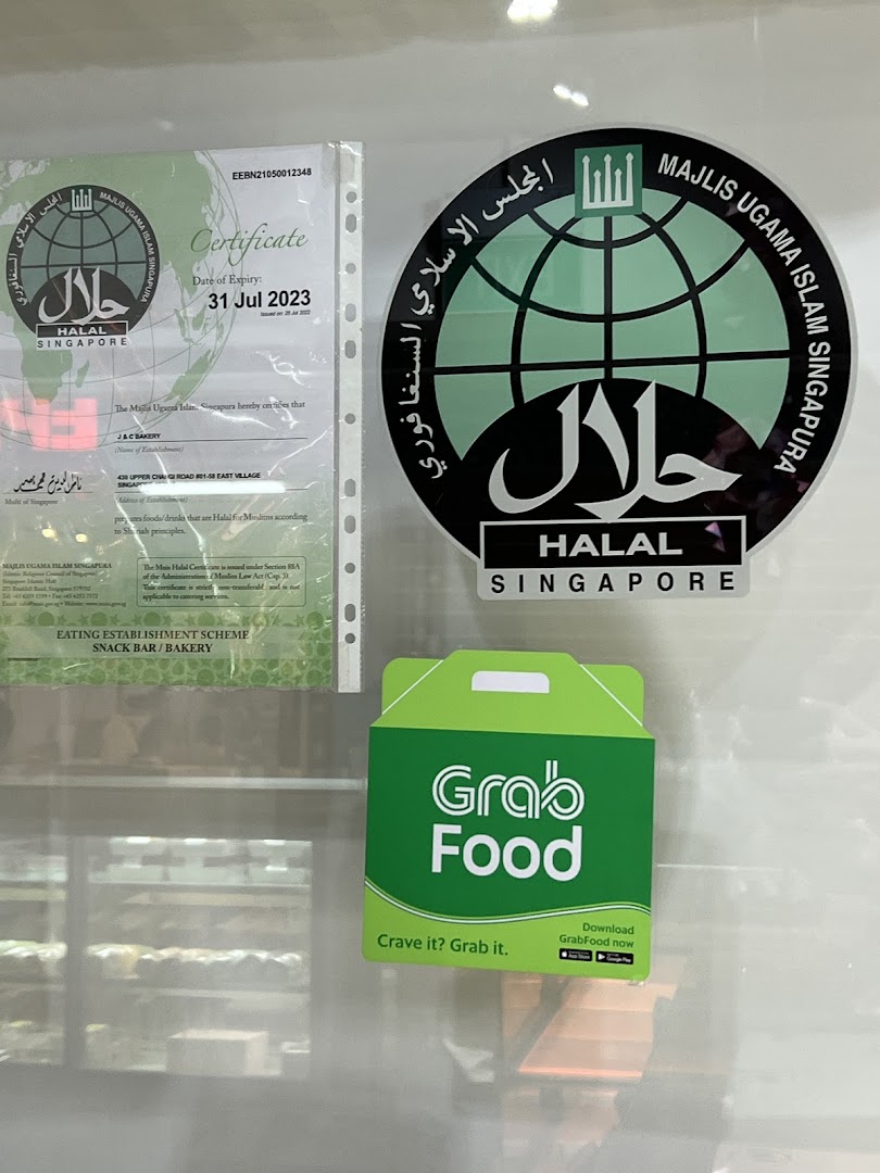 Halal certifications and a GrabFood sticker displayed on the window of J C Bakery.
