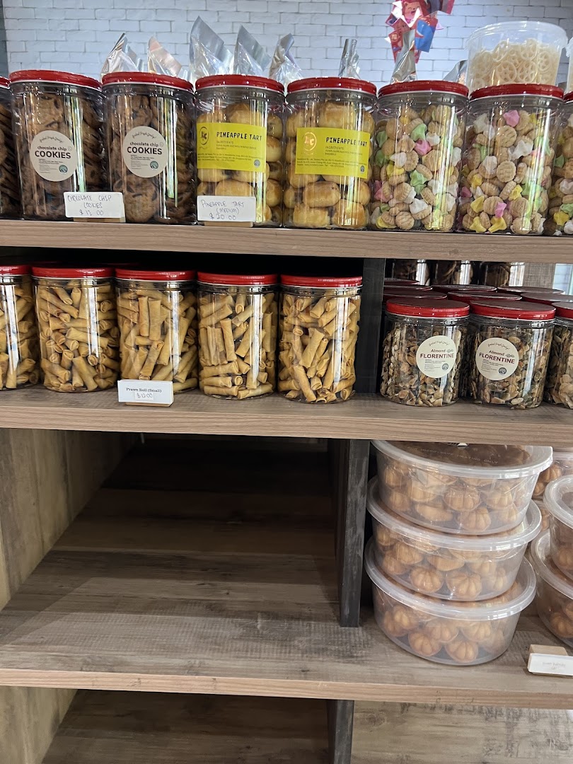 Shelves display various baked goods and snacks in clear containers, including cookies, pineapple tarts, and Florentines.