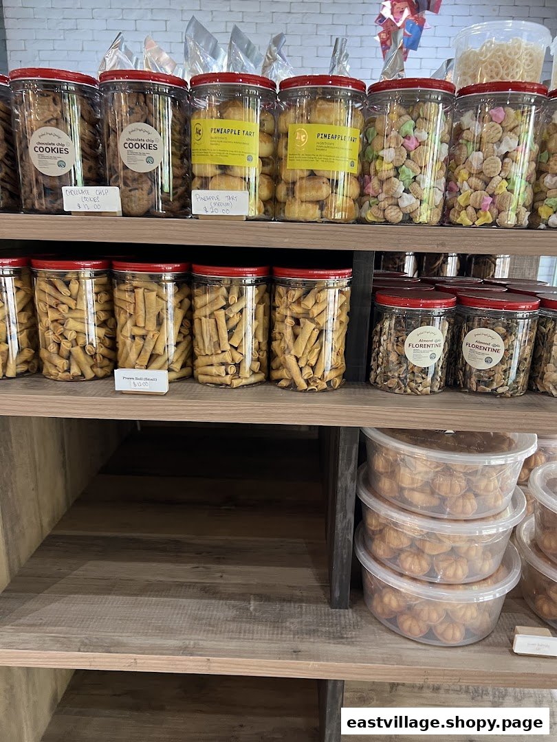 Shelves display various baked goods and snacks in clear containers, including cookies, pineapple tarts, and Florentines.