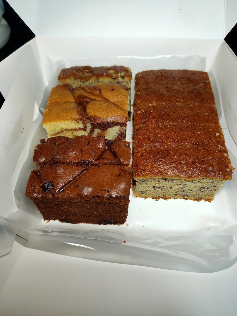 A white box filled with various sliced cakes and loaves, including marble, chocolate, and banana bread.