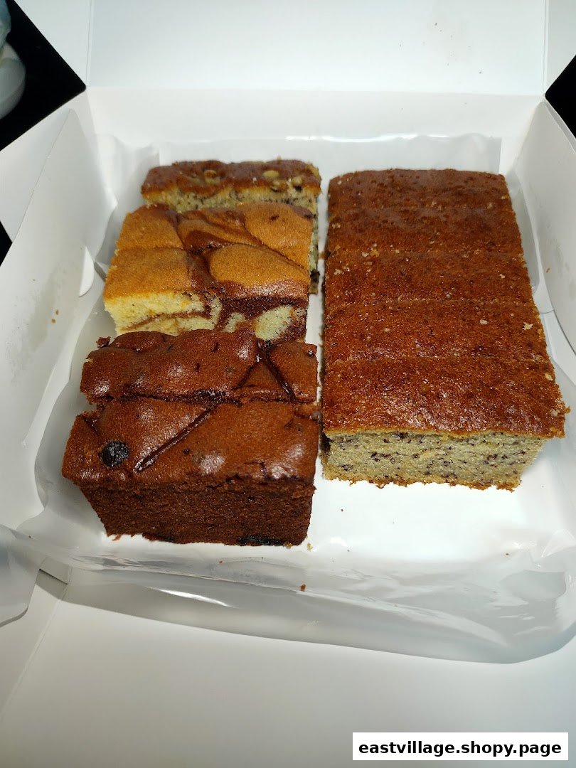 A white box filled with various sliced cakes and loaves, including marble, chocolate, and banana bread.