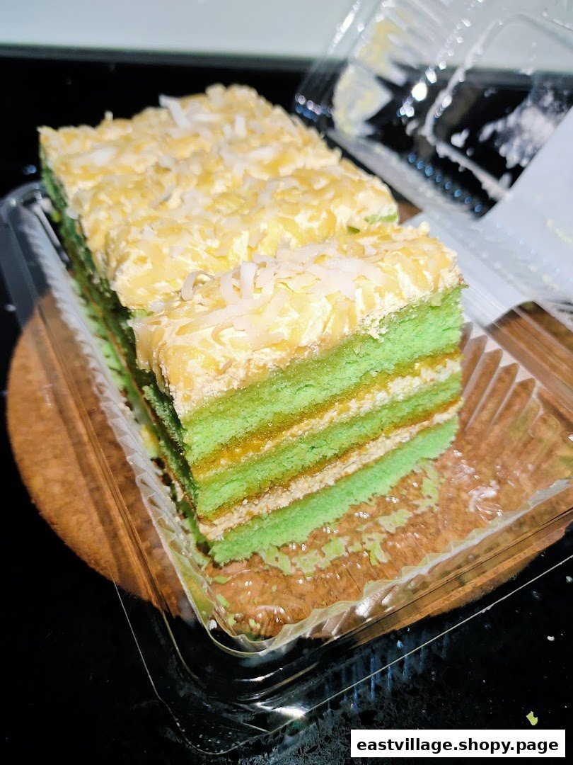 Close-up of layered green cake slices topped with coconut flakes in a clear plastic container.