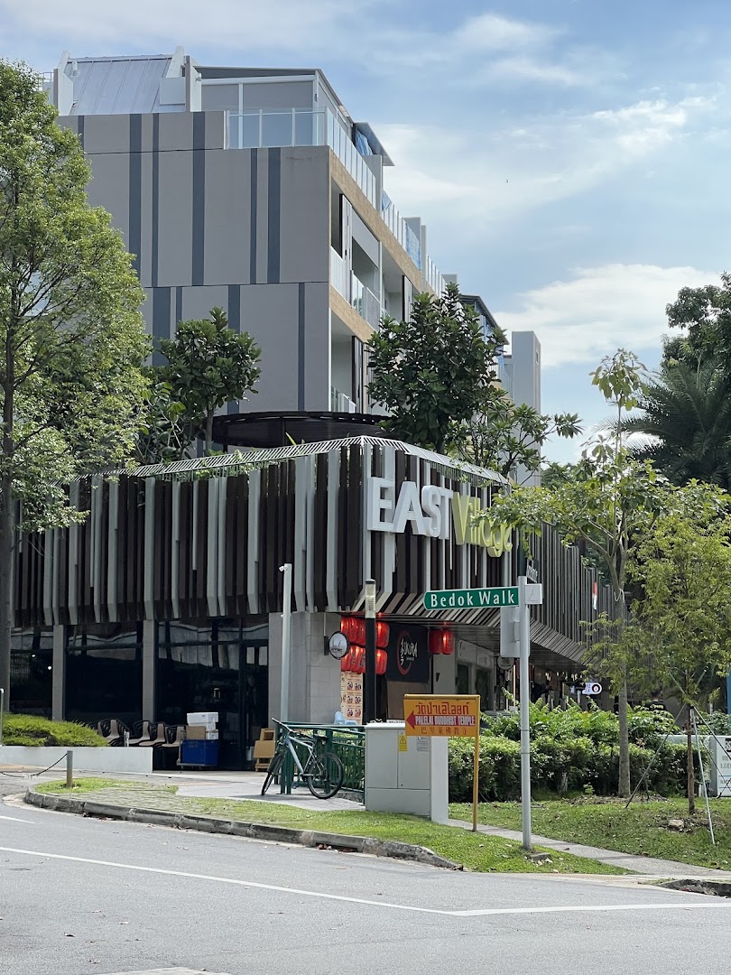 Exterior view of the modern 'EAST Village' building, featuring a shop entrance and lush greenery.