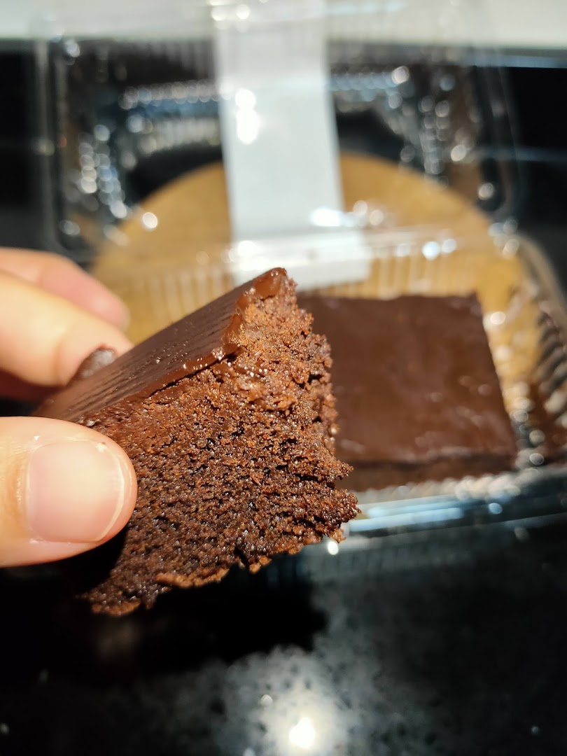 A hand holds a rich chocolate brownie, with another piece visible in a clear plastic container.