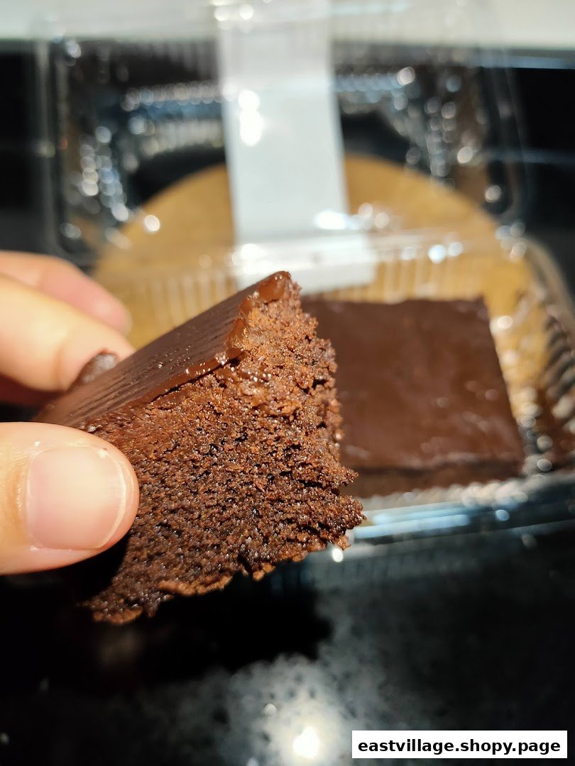 A hand holds a rich chocolate brownie, with another piece visible in a clear plastic container.