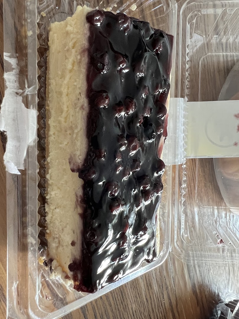A delicious slice of blueberry cheesecake in a clear plastic container.