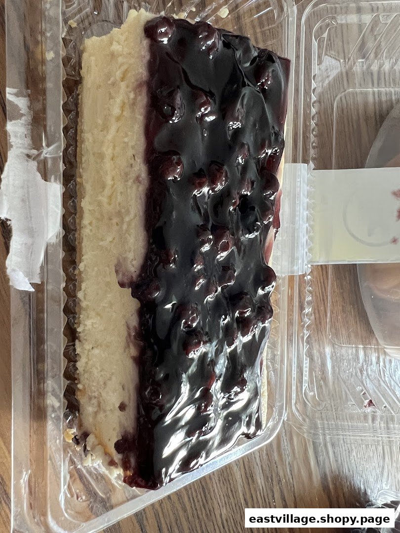 A delicious slice of blueberry cheesecake in a clear plastic container.