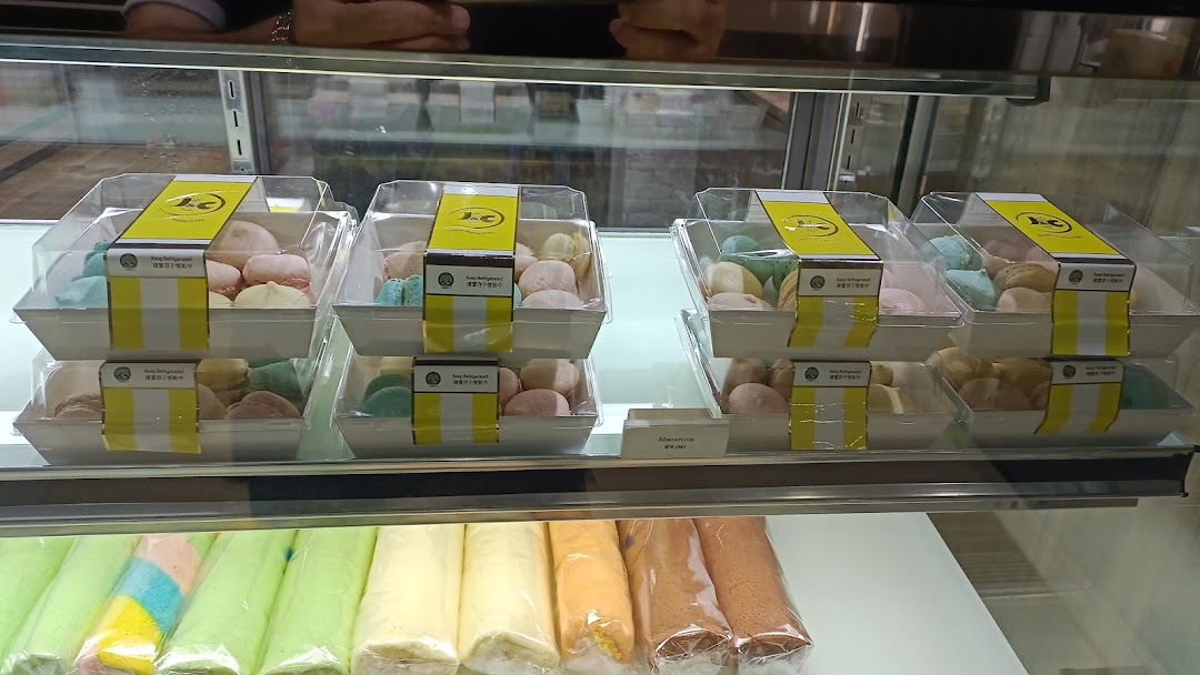 A display case filled with packaged mochi-like desserts and rolled cakes at J C Bakery.