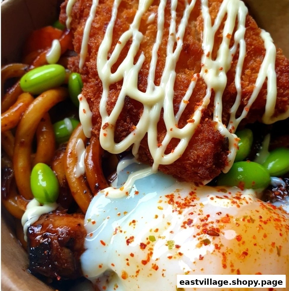 A close-up of a delicious Japanese-inspired dish featuring fried chicken, udon noodles, edamame, and a fried egg.