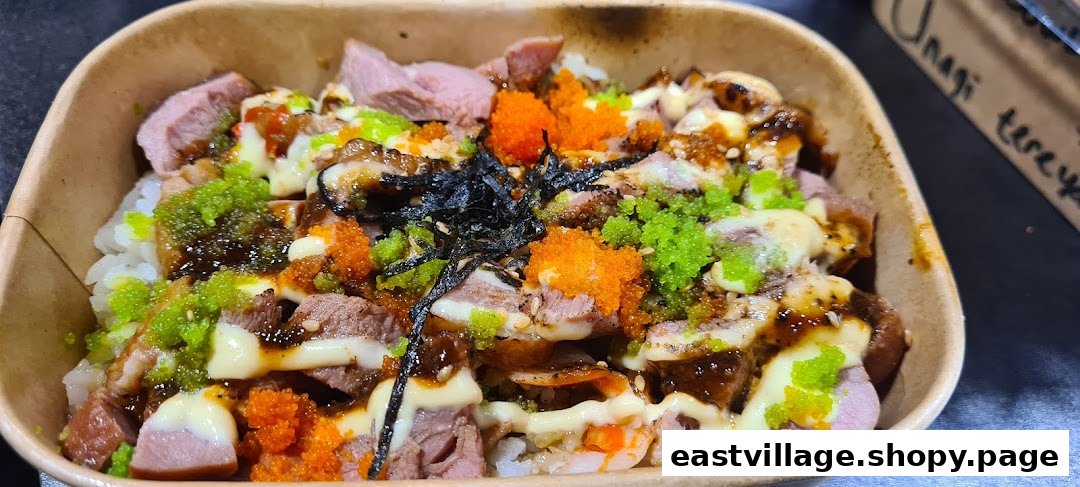 A vibrant rice bowl featuring sliced meats, colorful roe, seaweed, and creamy sauce in a paper container.
